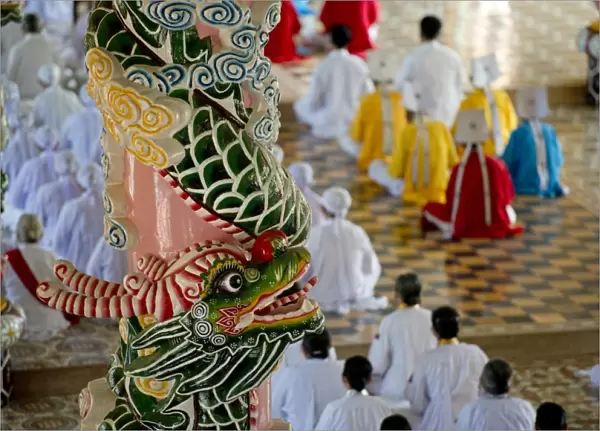 Caodaist disciples sitting beside colourful columns with dragons during ceremony, Cao Dai temple, Tay Ninh Holy See