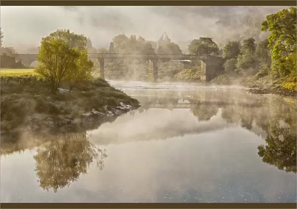 View of river, bridge and Cistercian abbey ruins in mist at dawn, Tintern Abbey, Tintern, River Wye, Wye Valley