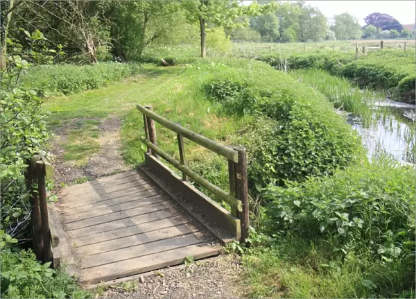 Wooden footbridge on footpath beside lowland river, River Rattlesden, Stowmarket, Suffolk, England, april