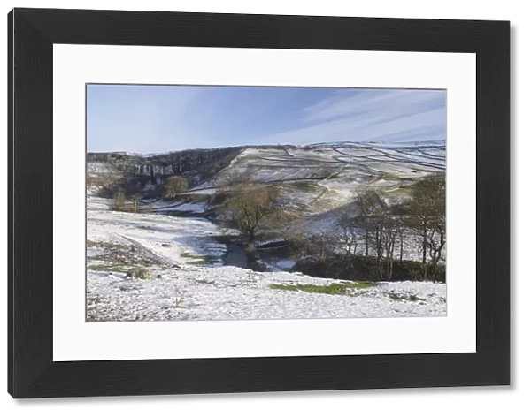 View of curved limestone cliff at head of valley, with stream flowing from base of cliff in snow, Malham Cove