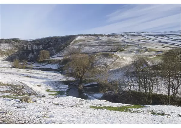 View of curved limestone cliff at head of valley, with stream flowing from base of cliff in snow, Malham Cove