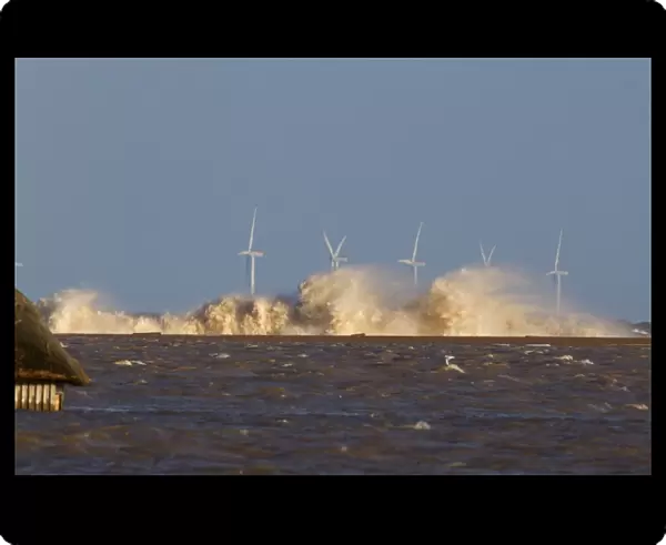 Waves crashing against remains of shingle sea defences, with flooded marshes