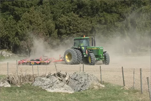 John Deere 4455 tractor pulling Vaderstad cultivator, cultivating arable seedbed, in dusty ploughed field, Sweden