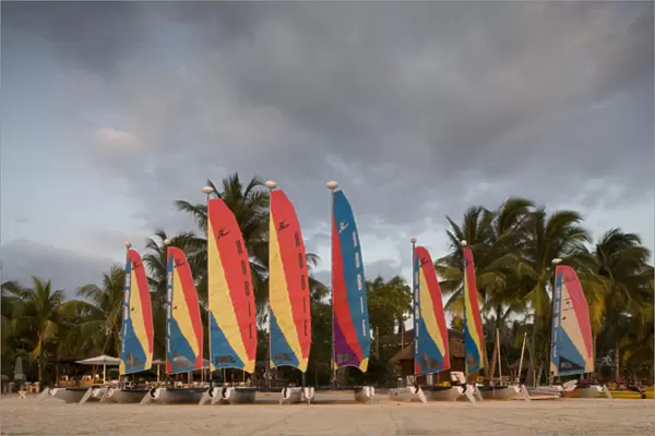 Jamaica, Negril, Setting sun lights row of sailboats at tourist resort along white