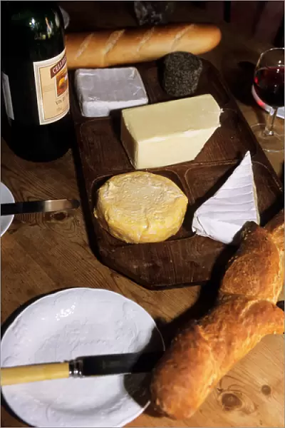 Brusvily, Britanny, France. Cheeses on a cheese board, bread, knife, bottle and glass