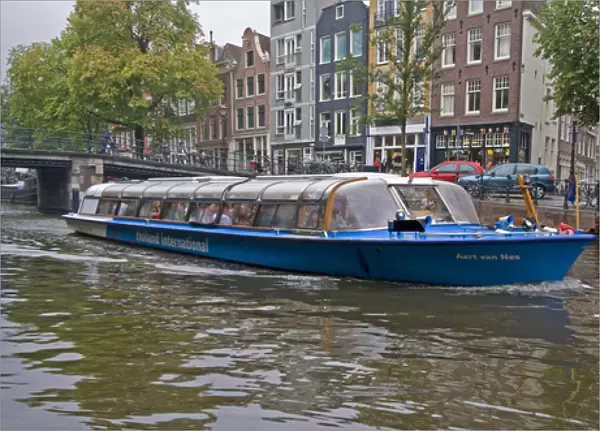 A tour boat full of people travel a canal lined with colorful gabled homes