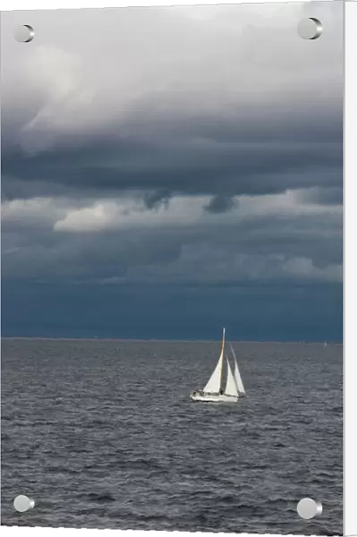 A small sailboat makes its way through the waters of Puget Sound under dark storm clouds