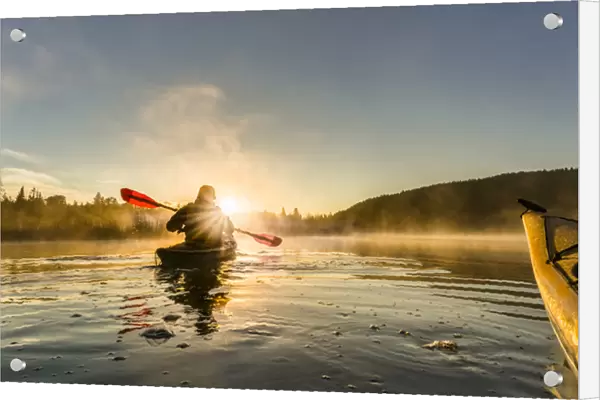 Canada, British Columbia. A kayaker paddles in sunlit early morning mist on a Canadian