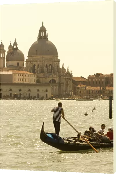 Italy; Venice. A gondolier ferries tourists on the Grand Canal in Venice with the massive church