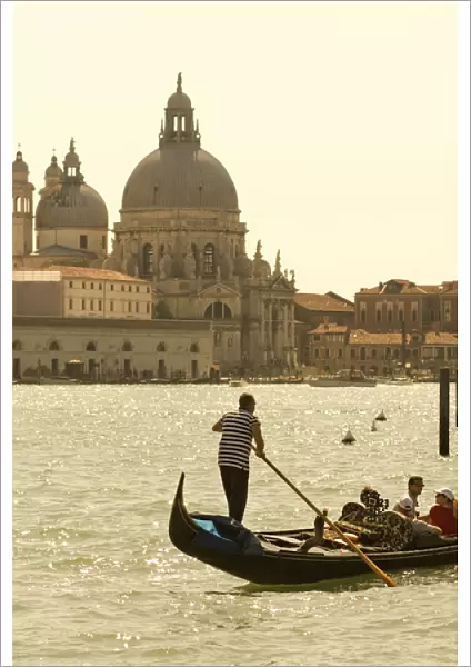 Italy; Venice. A gondolier ferries tourists on the Grand Canal in Venice with the massive church