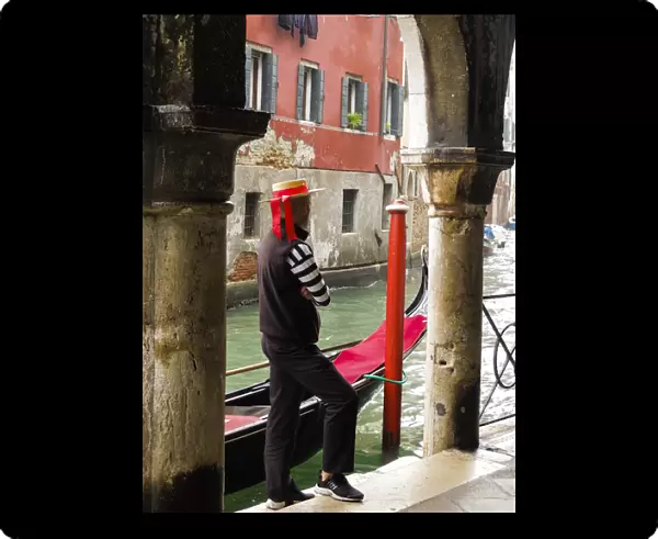 Venice, Italy. Gondolier man looks out onto the canal next to his gondola