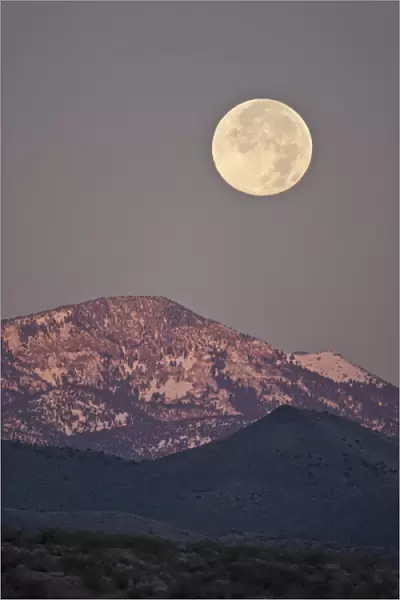 Full moon setting over snow-covered Magdelena Mountains at Socorro, New Mexico