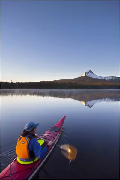 USA, Oregon. A woman in a sea kayak paddles at dawn on Big Lake, Oregon, in the Oregon Cascades
