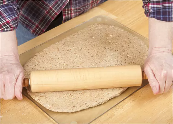 Woman rolling ball of bread dough with a rolling pin to flatten it, prior to forming