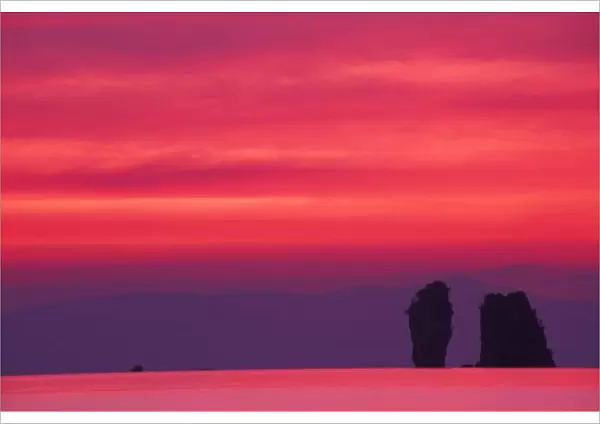 Thailand, Phang Nga Bay. Pink sky reflected in sea with jagged karst (limestone) islands