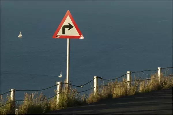 South Africa, Cape Town, Setting sun lights road sign warning of sharp turn along
