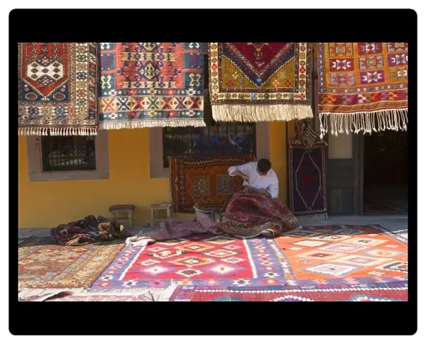 Man sewing the sides of a kilim in front of a local carpets shop, Pergamon (Pergamum