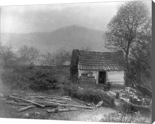 LOG CABIN, c1900. A man sitting in front of a small log cabin on a Sunday morning