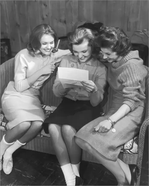 Three women sitting on sofa looking at letter