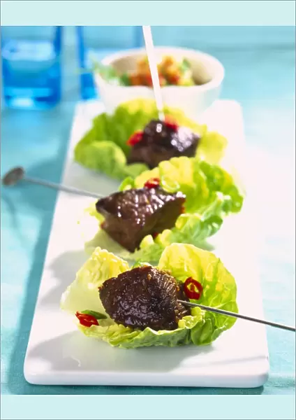 Three beef skewers served on individual lettuce leaves, close up