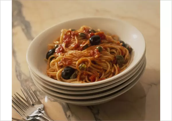 Spaghetti Puttanesca in bowl and a stack of bowls underneath