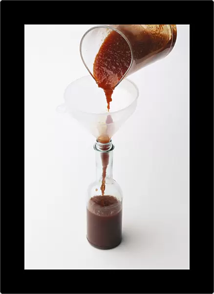 Pouring red chilli pepper ketchup through funnel into glass bottle