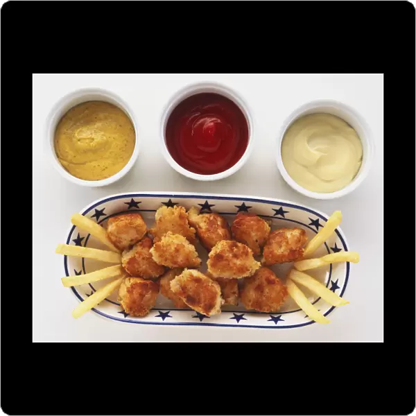 Above view of chicken nuggets, made with chicken coated in breadcrumb batter, on tray, with chips, accompanied with tomato ketchup, mayonnaise and mustard for dipping