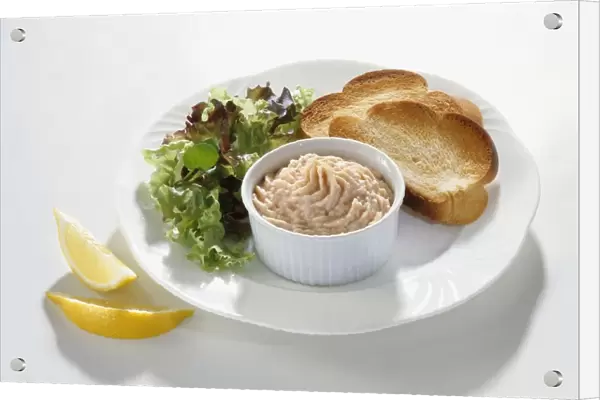 Smoked trout pate in ramekin served on white plate with toasted chollah and lettuce leaves and sliced lemon