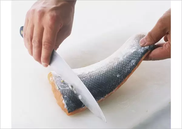 Close-up of a hand holding a knife on a salmon fillet