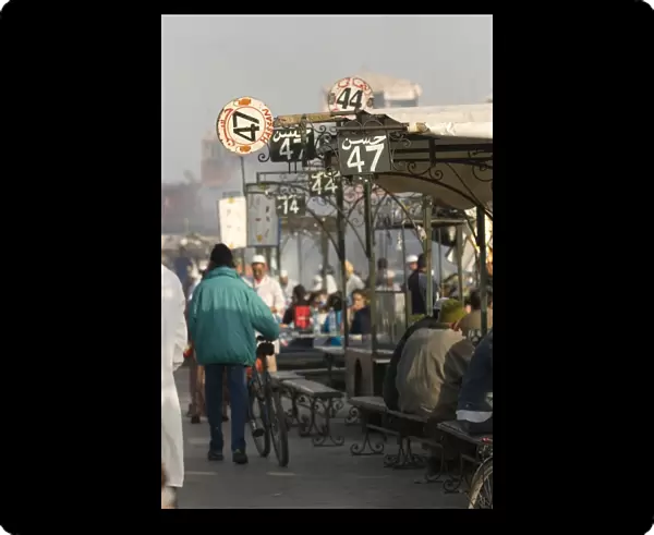 Morocco, Marrakech, Jemaa el Fna, people eating at food stalls, pedestrians walking past