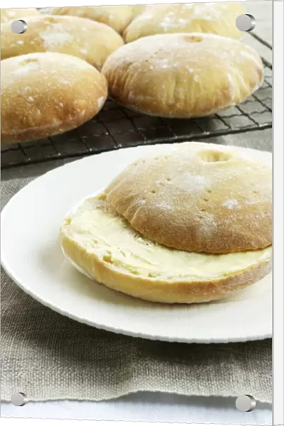 Stottie cakes, buttered on plate and on cooling rack nearby, a type of bread originally from Newcastle, Northeast England, close-up