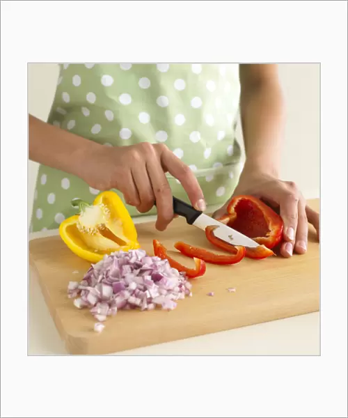 Woman slicing red pepper next to diced red onion and half yellow pepper