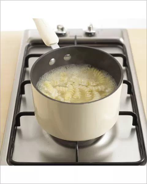 Bowl of fusilli pasta cooking in pan, close-up