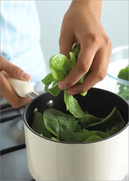 Woman adding raw spinach to saucepan