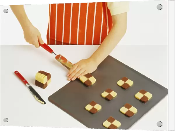 Hand model wearing orange and white striped apron, placing chocolate and plain shortbread dough