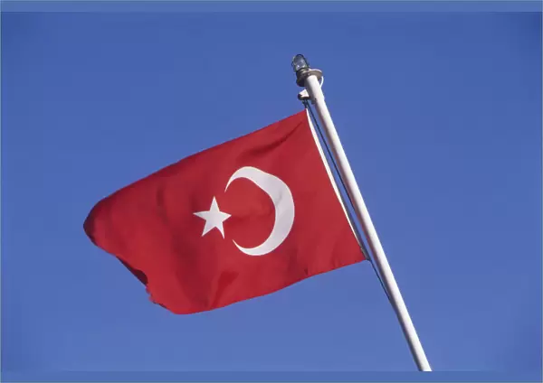 Turkish flag on white flagpole blowing in the breeze, deep blue sky in background