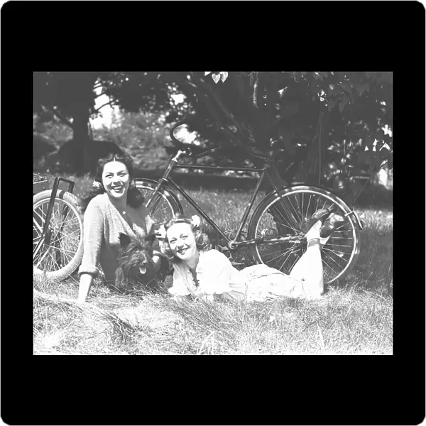 Two women and dog resting on grass, (B&W)