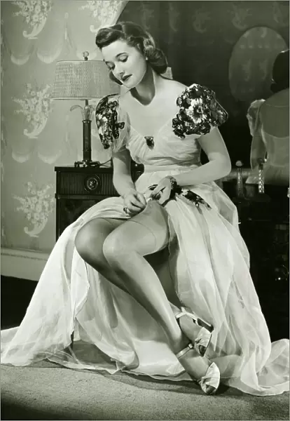 Glamorous woman in evening gown adjusting stockings, portrait, (B&W)