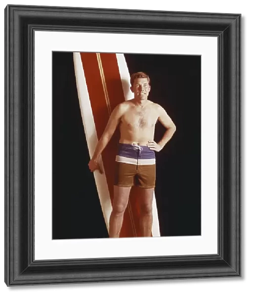 Mid adult man holding surfboard against black background