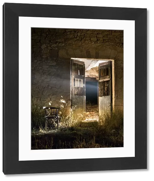 Door of a house in ruins opened in the night with a beam of light