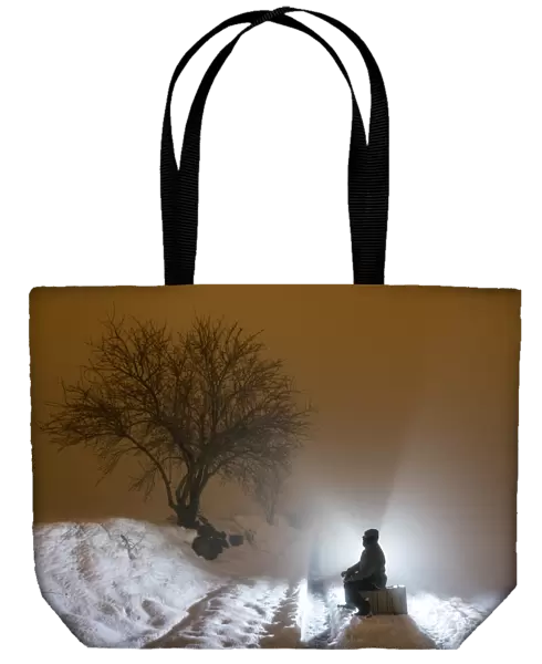 Silhouette of a person sitting on a suitcase resting, for a covered way of snow and fog during the night
