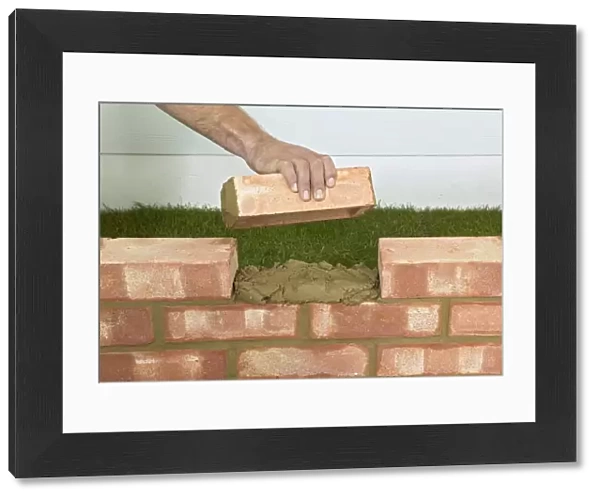 Hand holding brick above mortar between gap in wall, close up