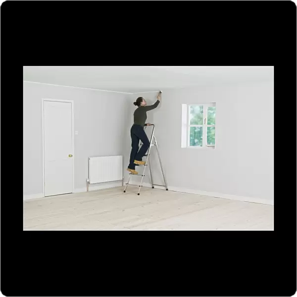 Woman on ladder painting edge of ceiling