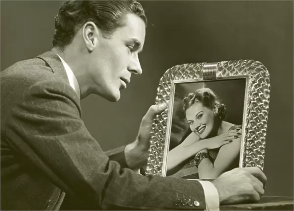 Man gazing at framed photo of woman