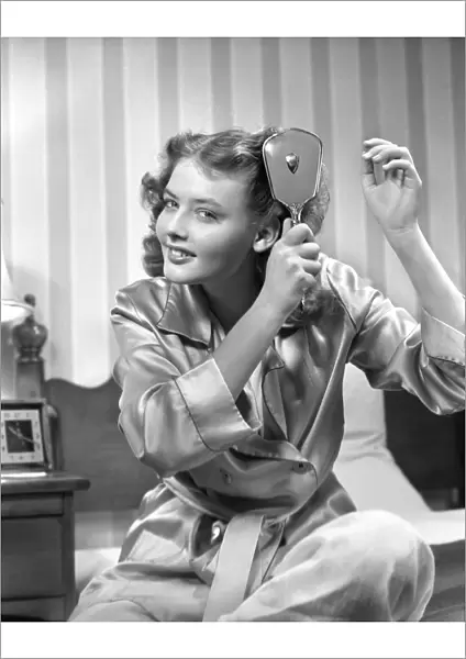 Smiling teenage girl in bathrobe brushing hair in the morning