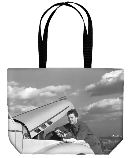 Smiling man in coveralls under hood of sedan, holding monkey wrench