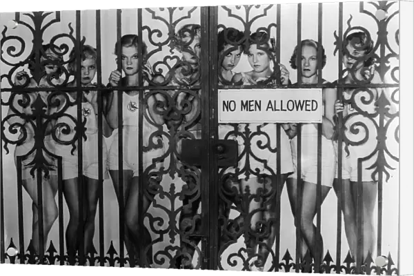 Fed Up. circa 1930: During filming in Hollywood girls pose behind wrought