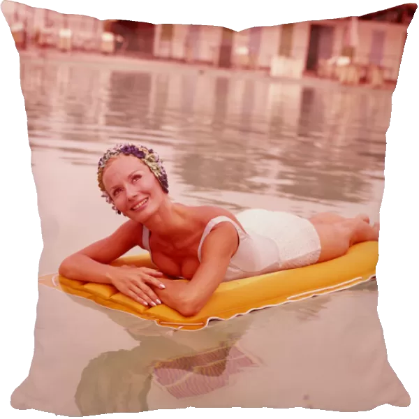 Woman in swimming pool reclining on inflatable raft, wearing bathing cap, smiling