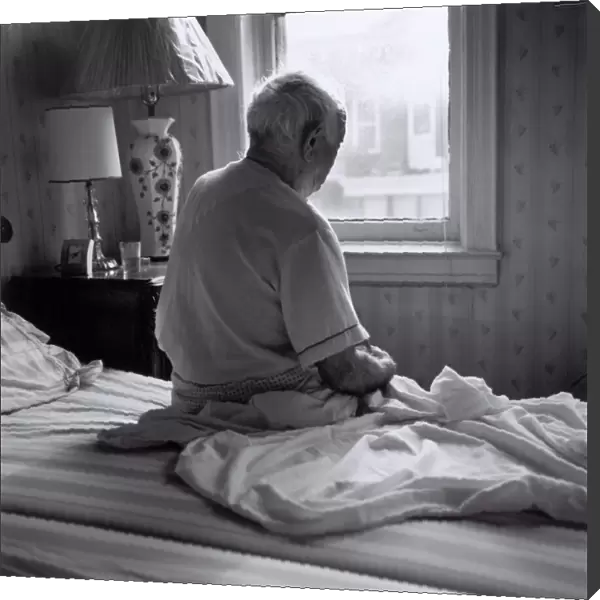 Senior man sitting on bed facing window