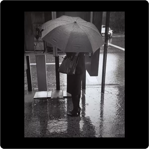 Woman with umbrella talking on public phone in rain